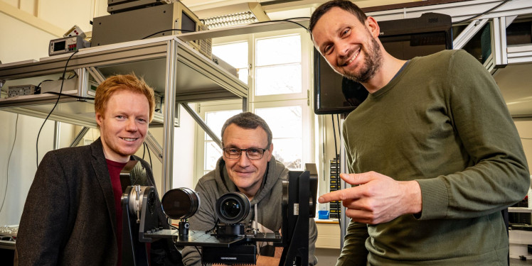 Drei Wissenschaftler stehen um einen optischen Laboraufbau herum